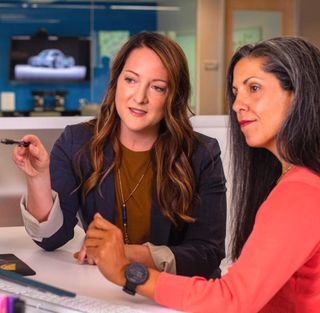 Two colleagues in conversation at a desk during a business meeting.
